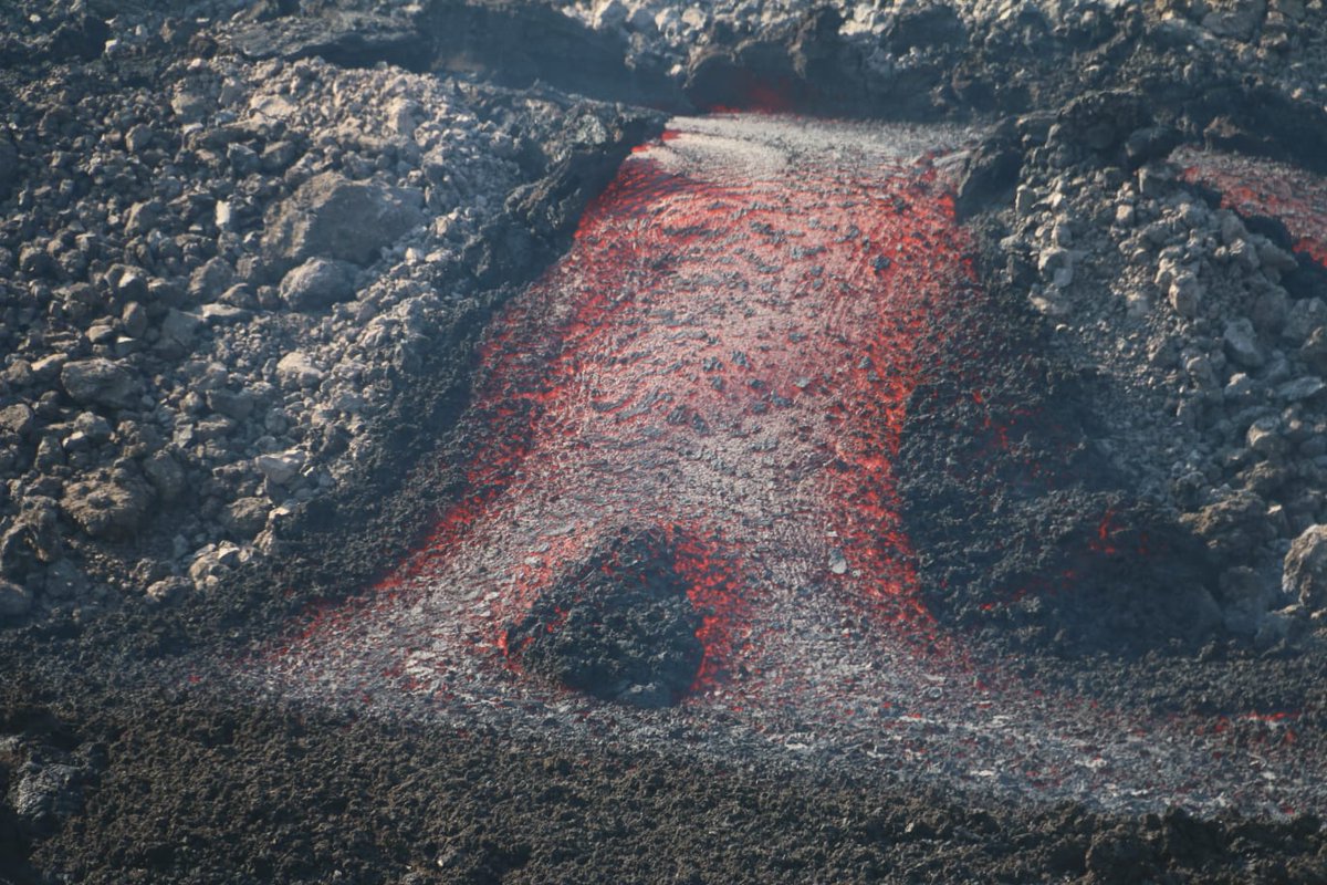 A flowing red river of lava seen flowing between levees of old cooled lava flows