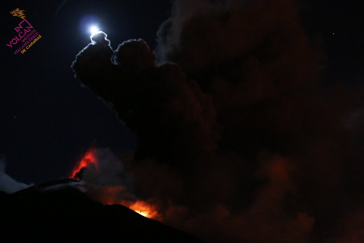 The volcano is silhouetted against the night sky and moonlight, with glowing areas of lava jets, and a thick ash cloud taking up most of the night sky in view 