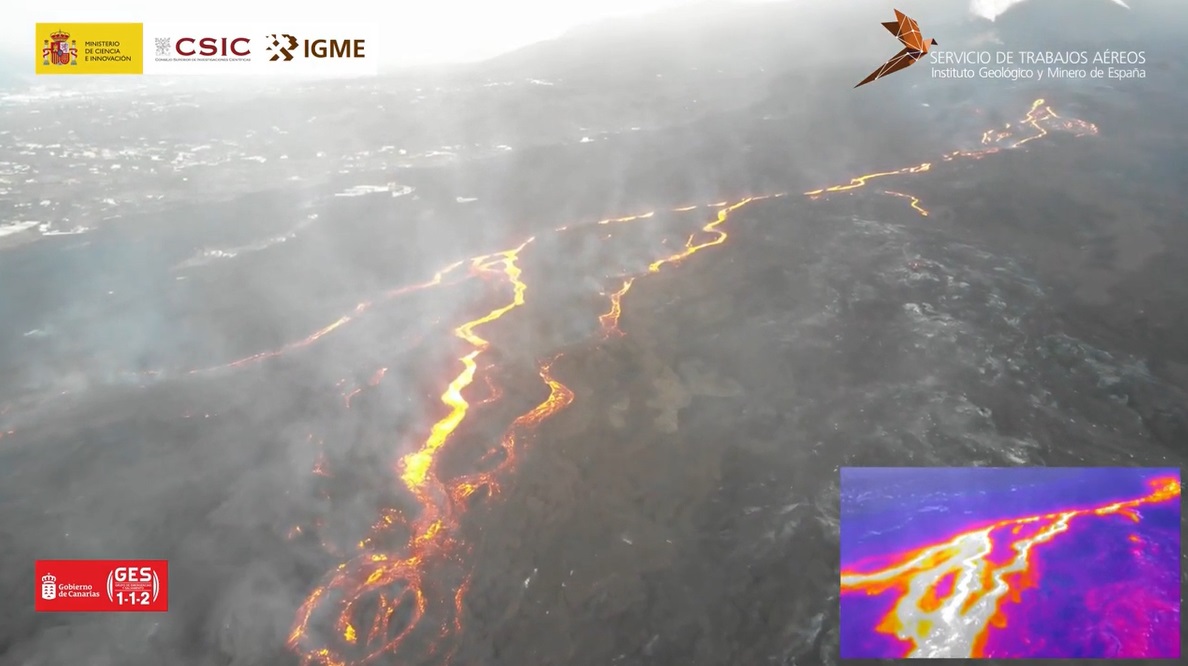 An image taken above the black lava flow field, with smoke rising from thin orange streams of the active lava flows that are flowing from right to left